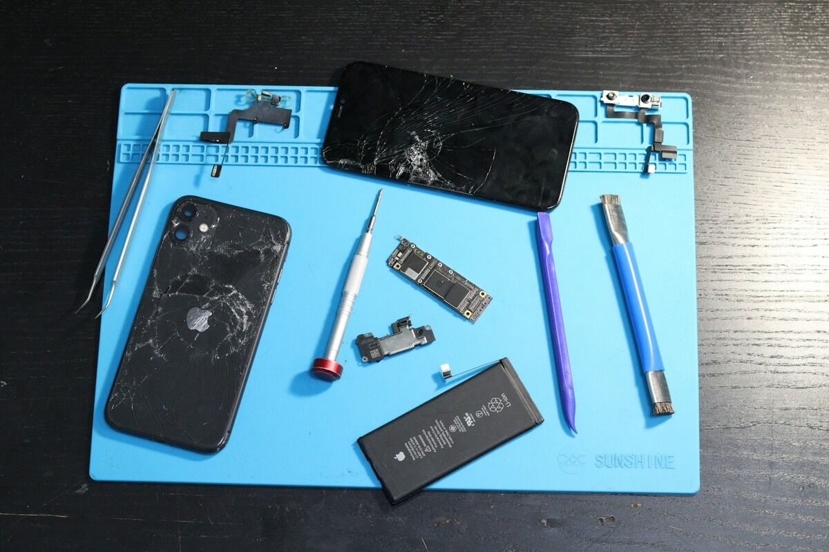 Smartphone démonté sur un tapis de réparation, batterie et outils posés à côté