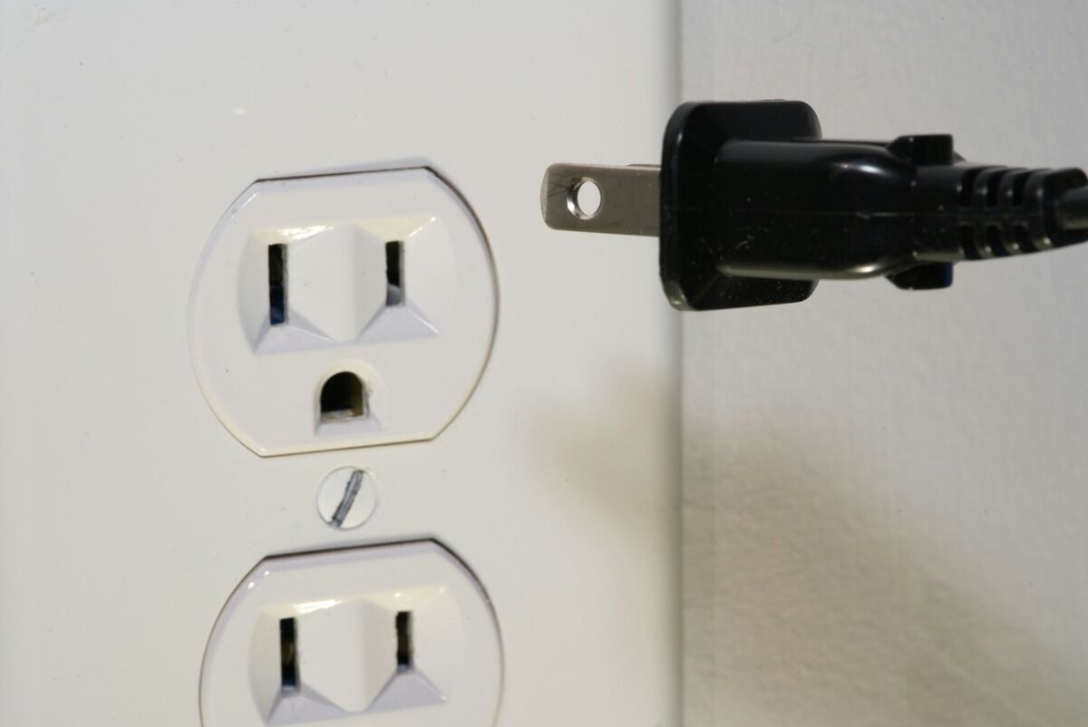 Fiche électrique noire tenue devant une prise murale