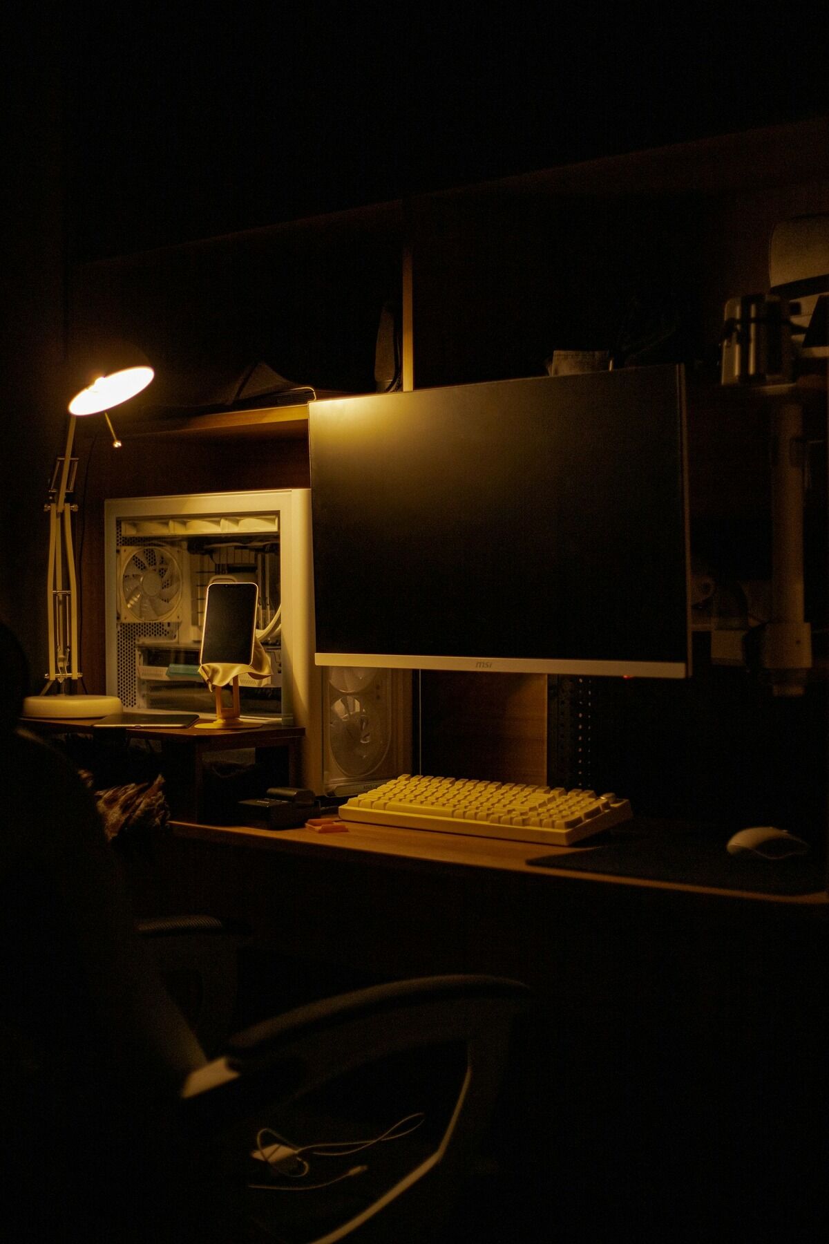 Bureau avec écran et clavier dans une pièce sombre éclairée par une lampe