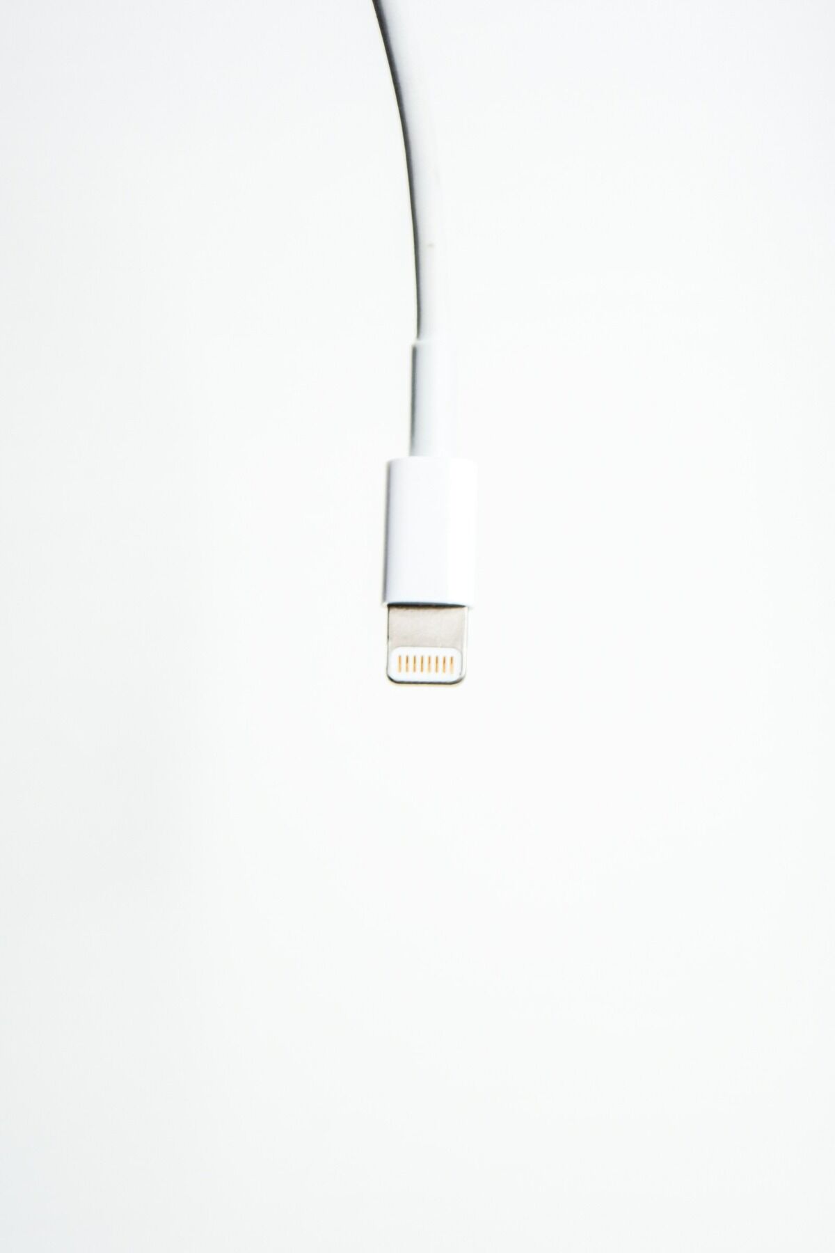 Connecteur Lightning blanc d'un câble de recharge d'iPhone, suspendu sur fond clair