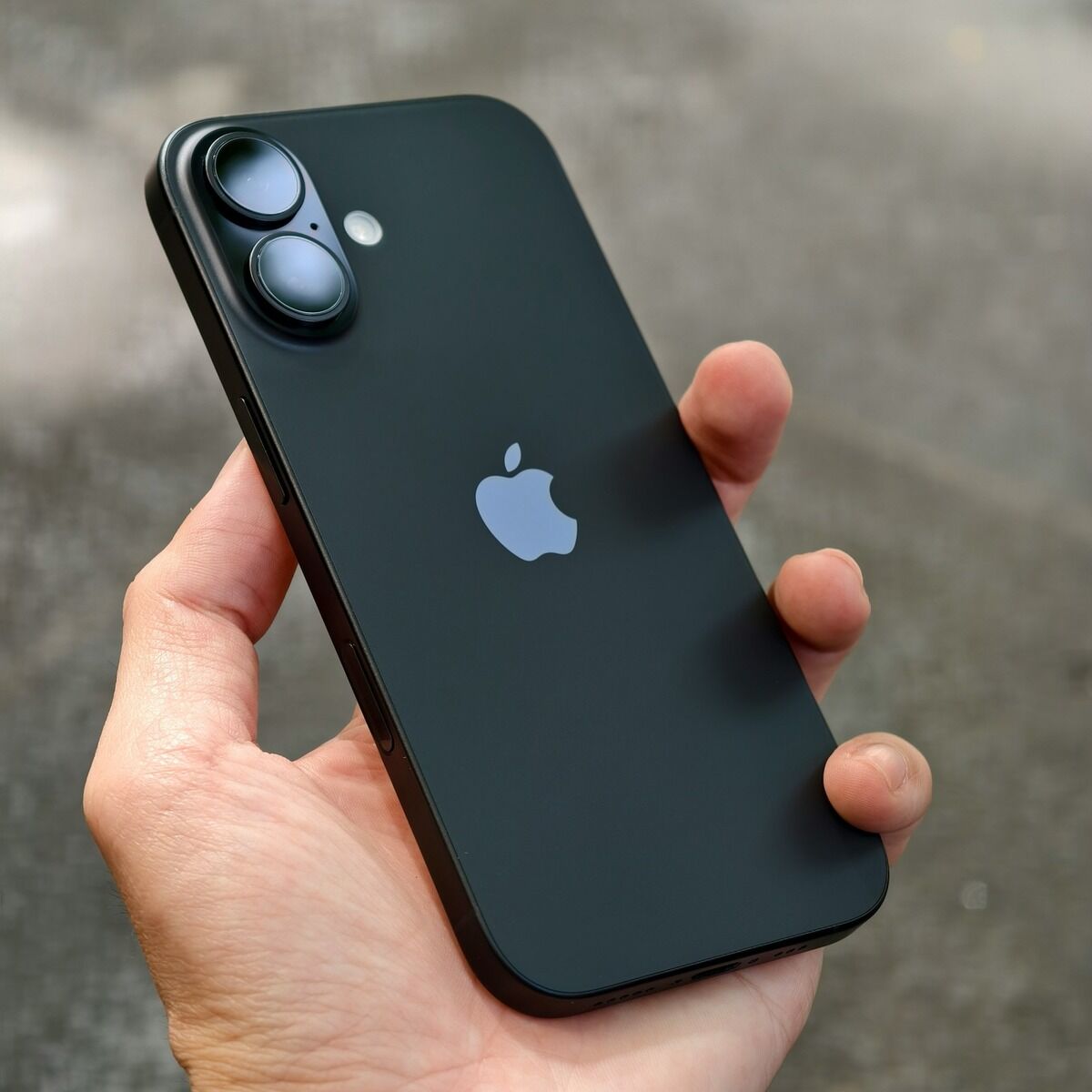 Main tenant un iPhone récent, dos noir et bloc photo à deux objectifs