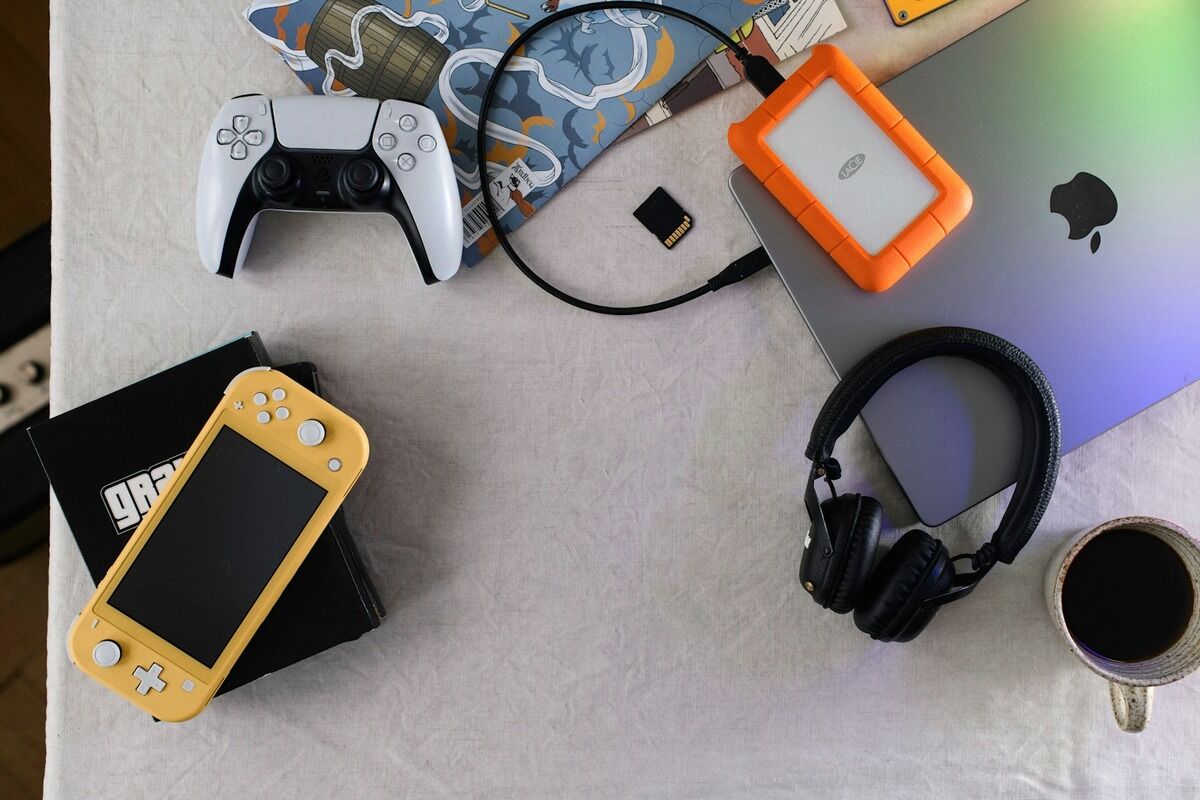 Manette de jeu, console portable, casque et disque externe posés sur un bureau clair