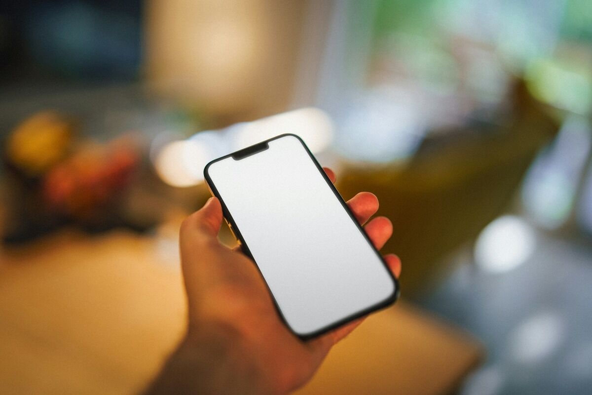 Main tenant un smartphone à l'écran blanc