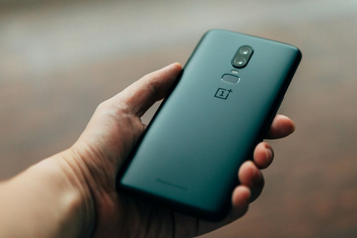 Main tenant un smartphone Android, dos vers l'objectif, sur fond flou