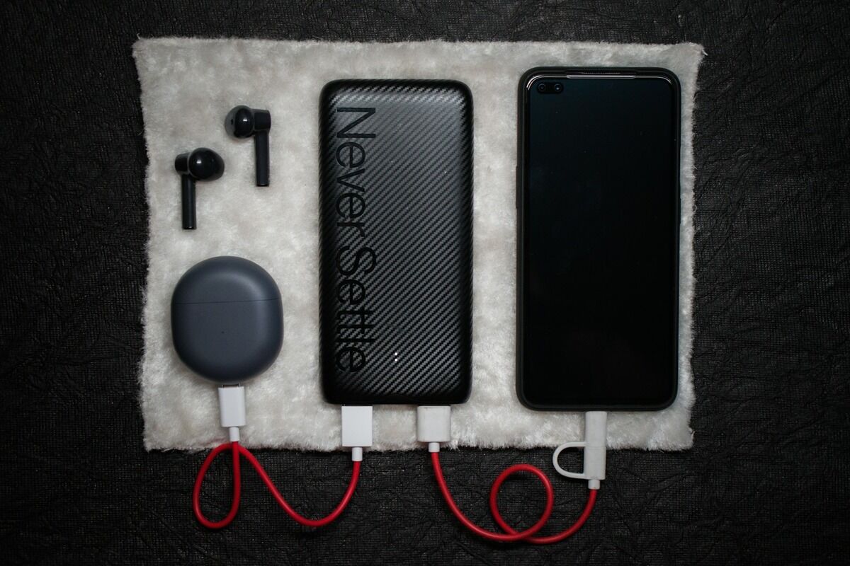 Smartphone noir, câble USB blanc et écouteurs posés côte à côte