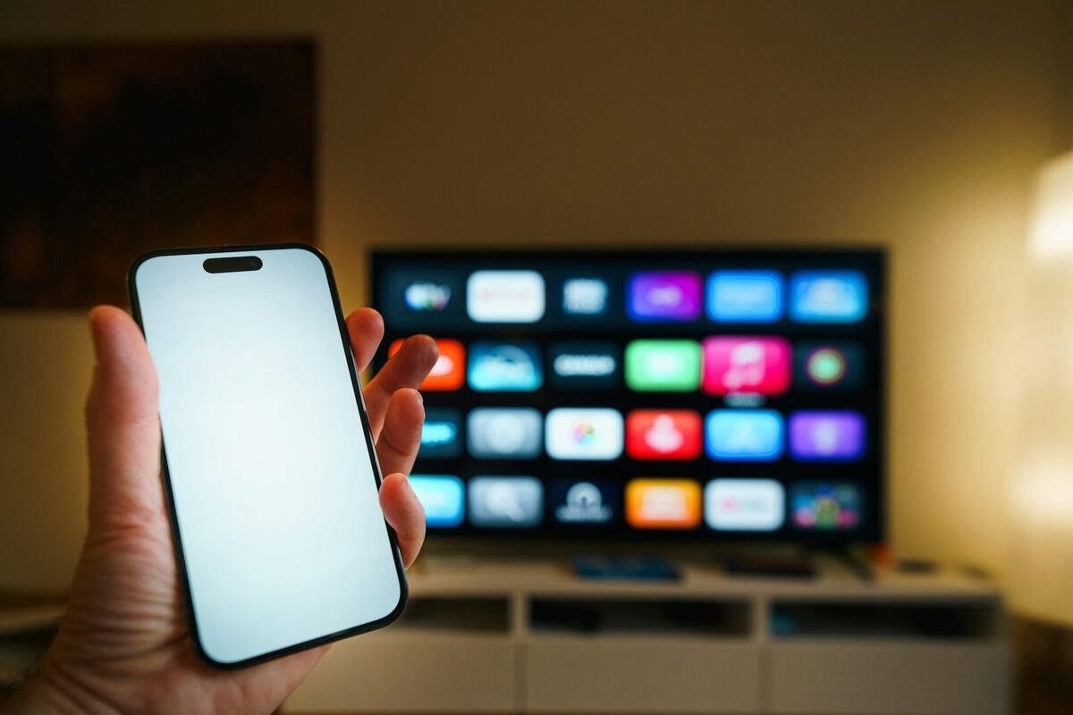 Main tenant un smartphone devant un grand téléviseur dans un salon